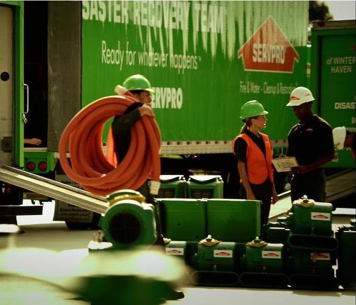 img src =”team” alt = " group of 3 SERVPRO reps standing near a green semi truck at a work site ” >